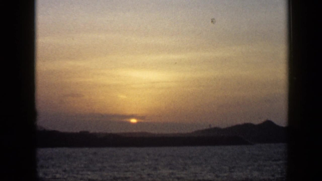 1959 Venezuela 8mm frame with the sun dimmed by cloud cover above a lake or broad waterway and low hills.