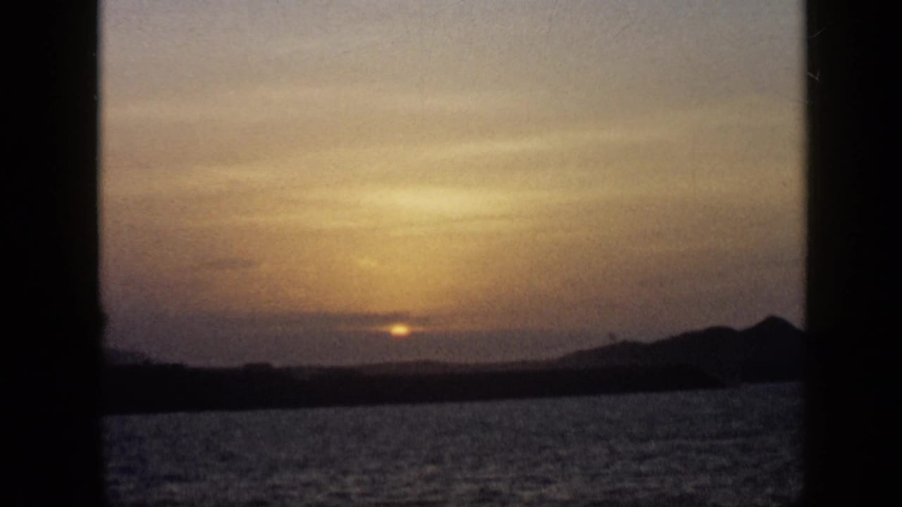 1959 Venezuela 8mm sunset view with softened light, rippled water, and a dark mountain silhouette at the right horizon.