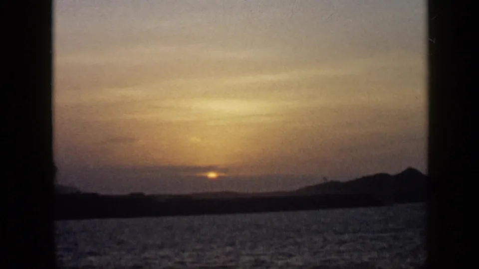 1959 Venezuela 8mm sunset view with softened light, rippled water, and a dark mountain silhouette at the right horizon.