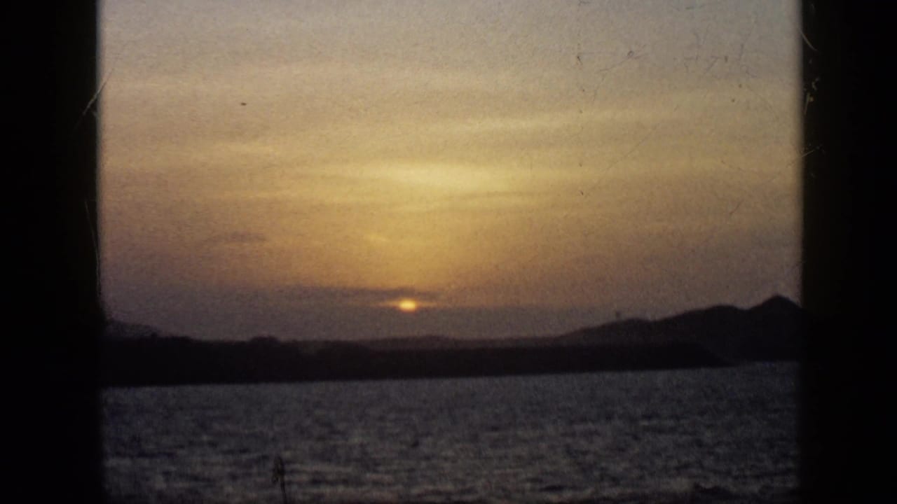 1959 Venezuela 8mm frame showing the sun near the horizon over water, with silhouetted mountains and dark framing bars.