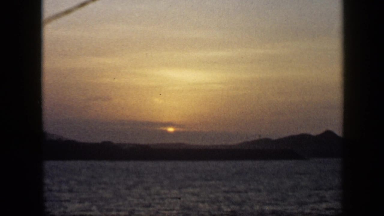 Low sun over water and silhouetted mountains behind dark vertical frame bars.