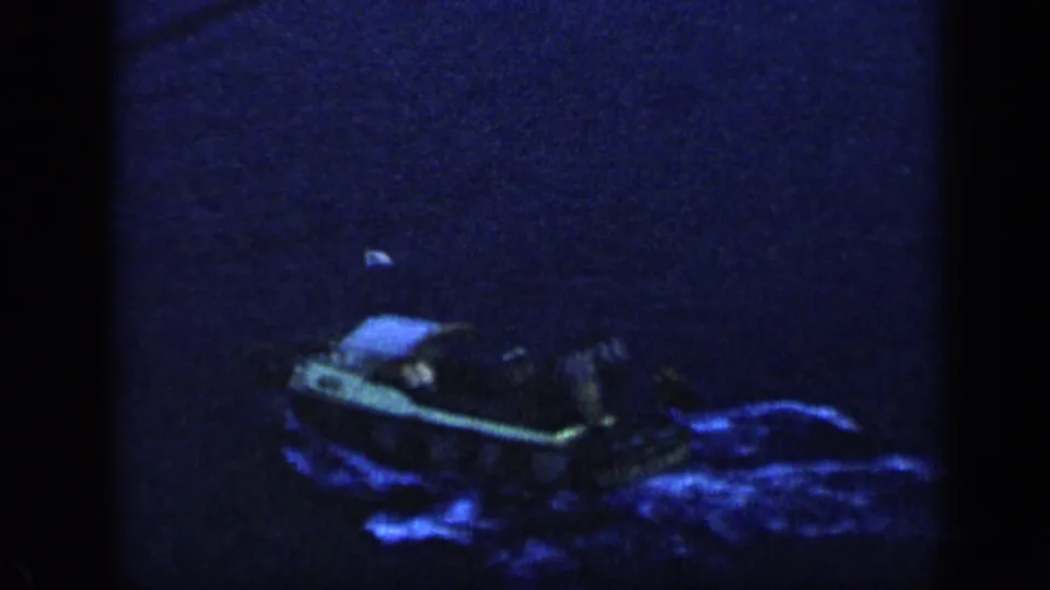 Overhead home-movie view of a small boat in dark Venezuelan water with a blue luminous trail.