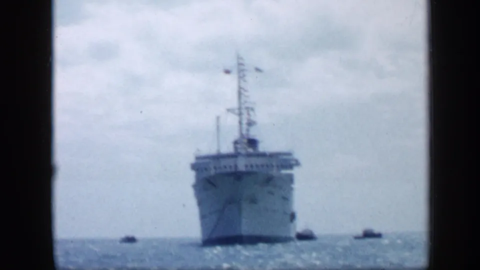 1959 Venezuela home-movie frame showing a large ship offshore with small boats around it on open water.