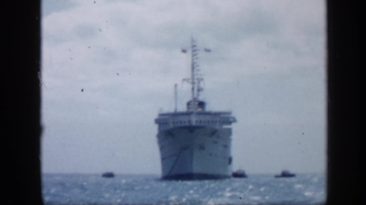 Large ship approaching across open water with small tugboats nearby.