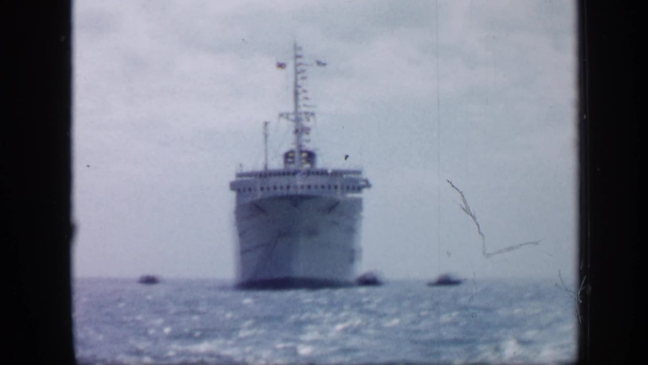1959 Venezuela frame of a large ship facing the camera on open water, with tugboats positioned near the hull.