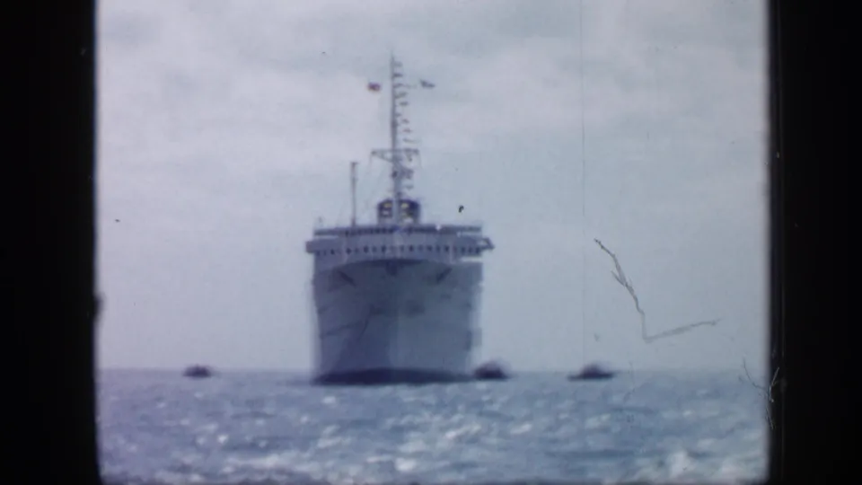 1959 Venezuela frame of a large ship facing the camera on open water, with tugboats positioned near the hull.