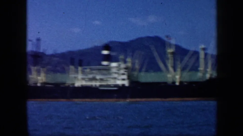 1959 Venezuela harbor frame showing a cargo ship near dock structures with mountains in the background.