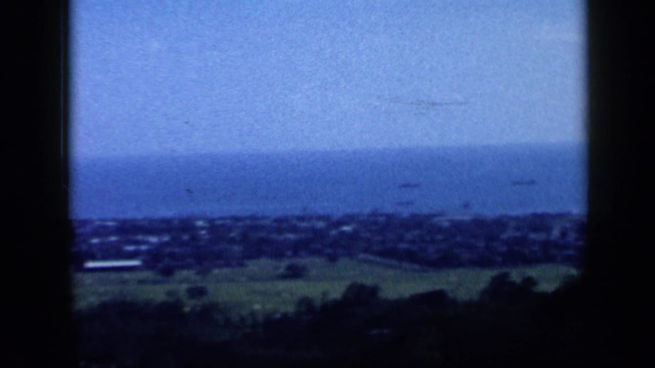 1959 Venezuela coastal overlook with a distant town, open water, and hazy horizon below the hill.