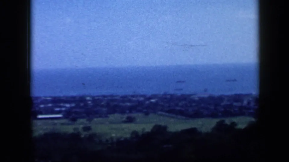 1959 Venezuela coastal overlook with a distant town, open water, and hazy horizon below the hill.