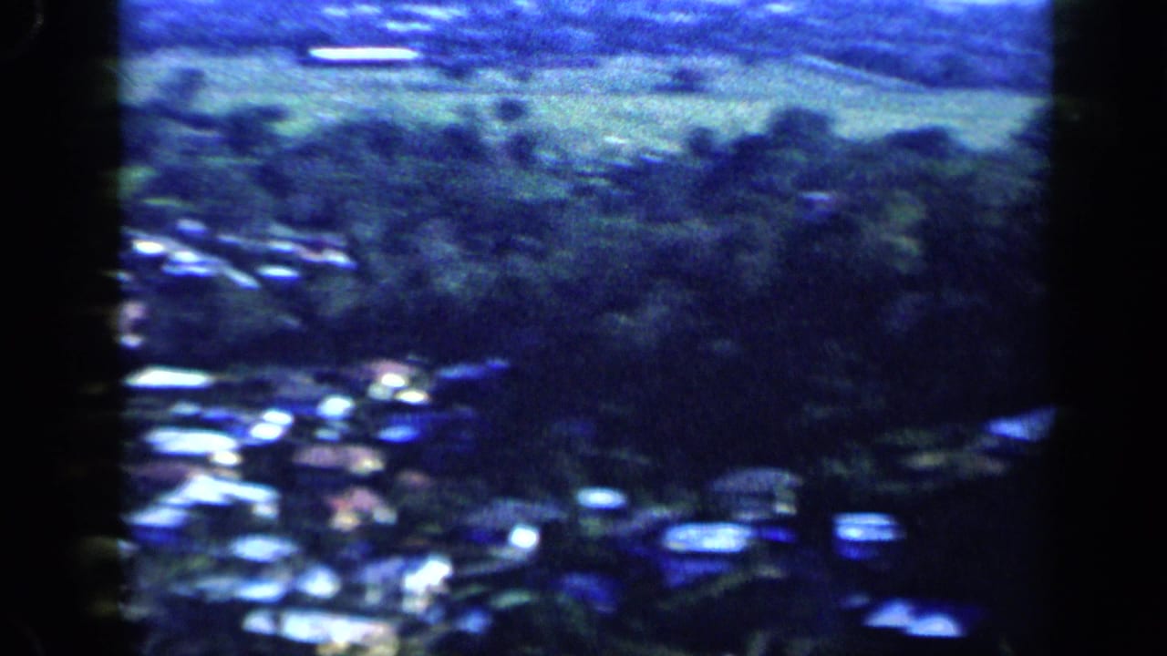 Distant houses and trees on a green hillside seen from an elevated viewpoint.