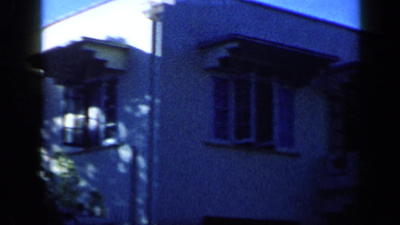 White residential exterior with windows and roof edges, filmed in 1959 Venezuela from a nearby upstairs vantage point.