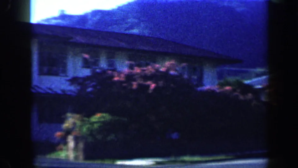 1959 Venezuela 8mm frame showing a house exterior, garden shrubs, and hillside backdrop in soft saturated home-movie color.