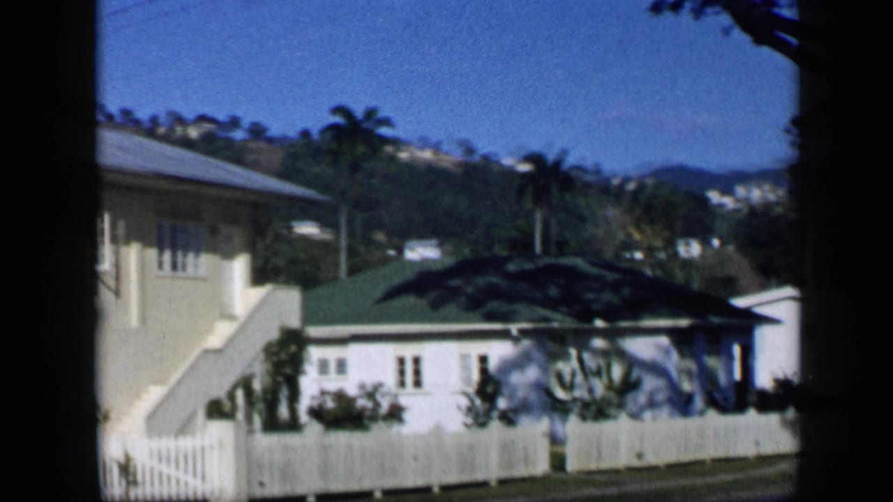 House exterior with stairs, white fence, small outbuilding, palms, and distant hillside.