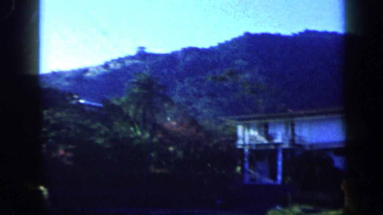 1959 Venezuela 8mm frame showing a fast passing view of a hillside, trees, and a house exterior.