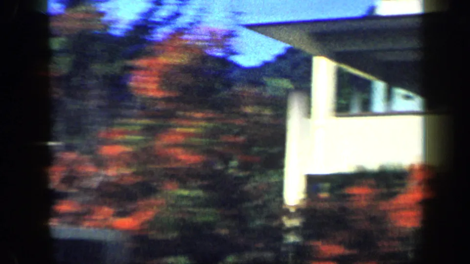 1959 Venezuela 8mm frame with a white residential exterior and red flowering shrubs during a fast drive-by.
