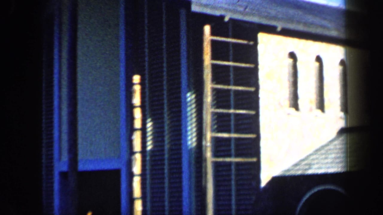 1959 Venezuela home-movie frame of a sunlit house facade with tall shutters, rectangular windows, and a roof edge.