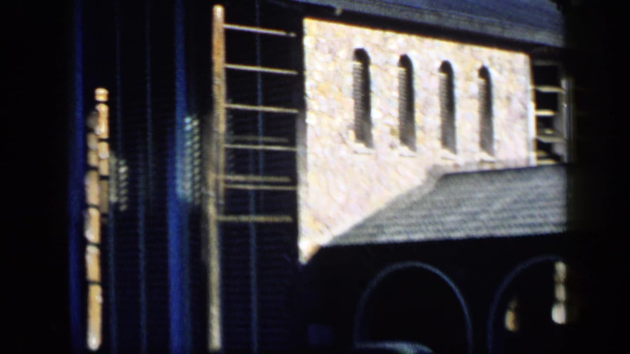 1959 Venezuela home-movie frame showing a textured building facade with arches, a tiled roof, tall windows, and strong daylight contrast.
