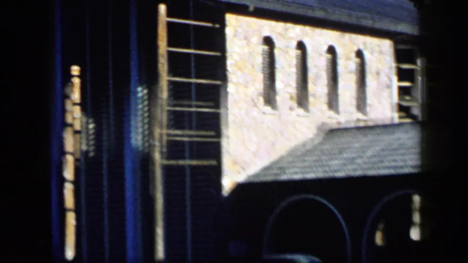 1959 Venezuela home-movie frame showing a textured building facade with arches, a tiled roof, tall windows, and strong daylight contrast.