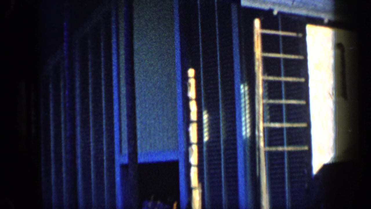 1959 Venezuela home-movie frame with a close pan past tall windows, dark facade edge, blue shadow, and sunlit textured wall.