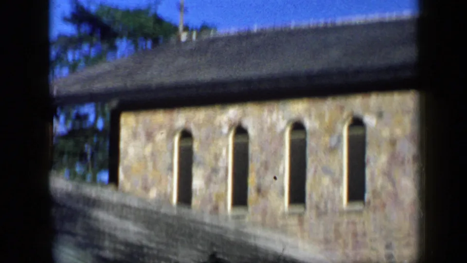 1959 Venezuela 8mm view of a traditional stone building with tall arched windows, sloped roof, and trees above the roofline.