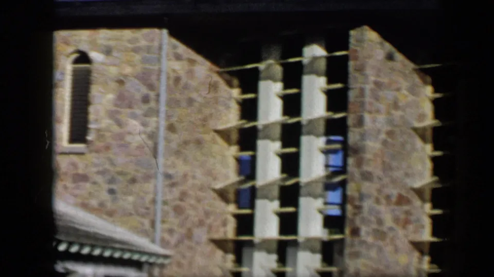 1959 Venezuela frame showing a stone facade with an arched window, sloped roof edge, and scaffolding or exterior framework.