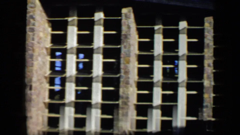 1959 Venezuela frame showing repeated white-framed windows across a stone facade with dark shadowed areas at the edges.