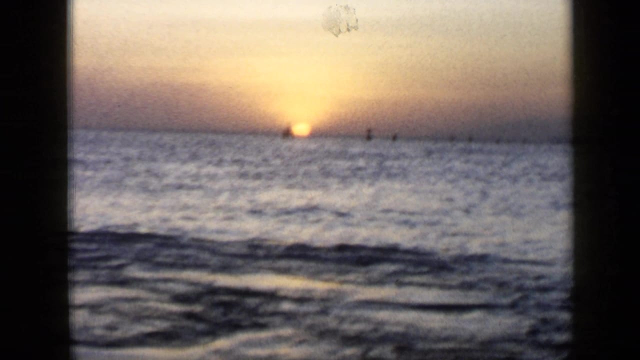 Low sun sits on the ocean horizon with small distant silhouettes on the water.