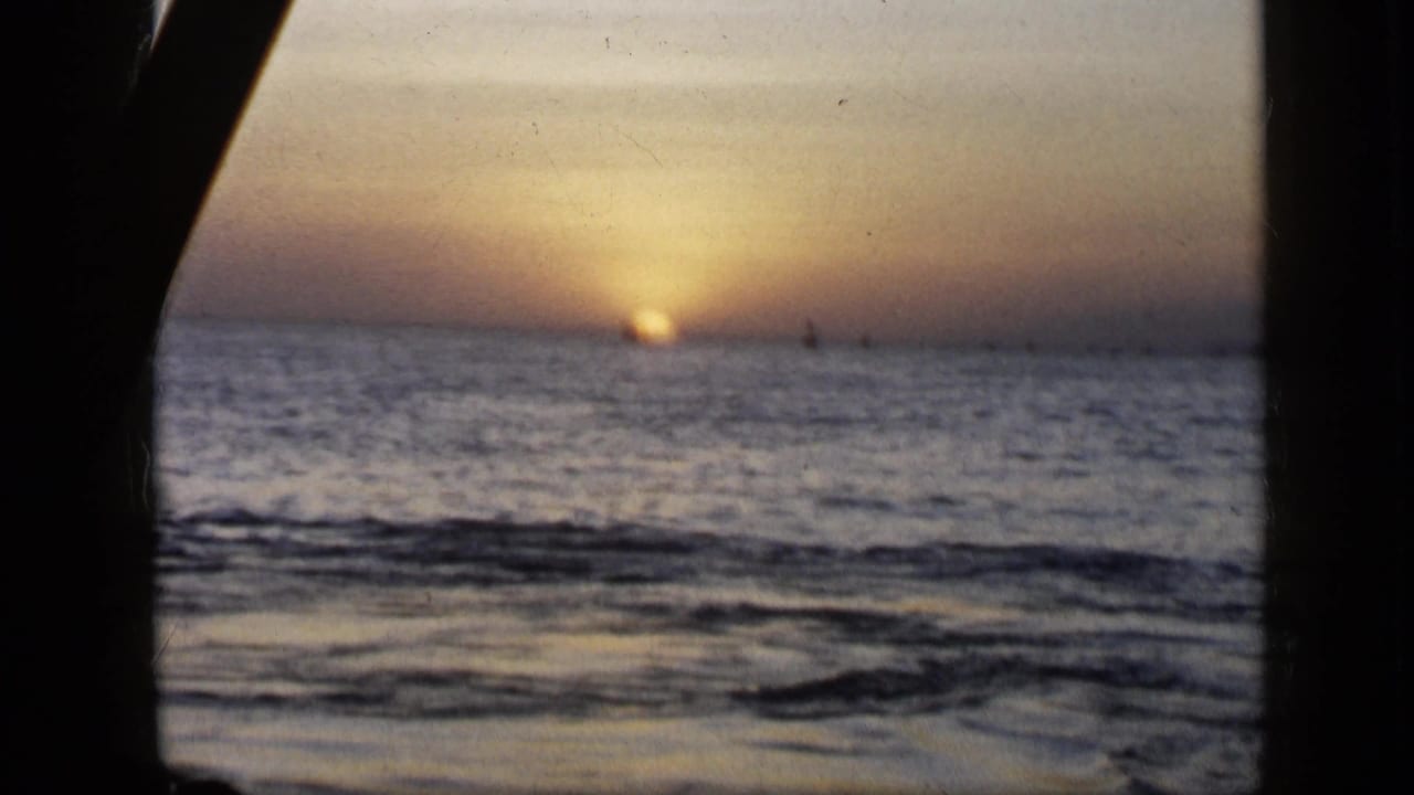A second 1959 Venezuela home-movie view of the sun setting over rippled ocean water, with a dark frame edge at left.