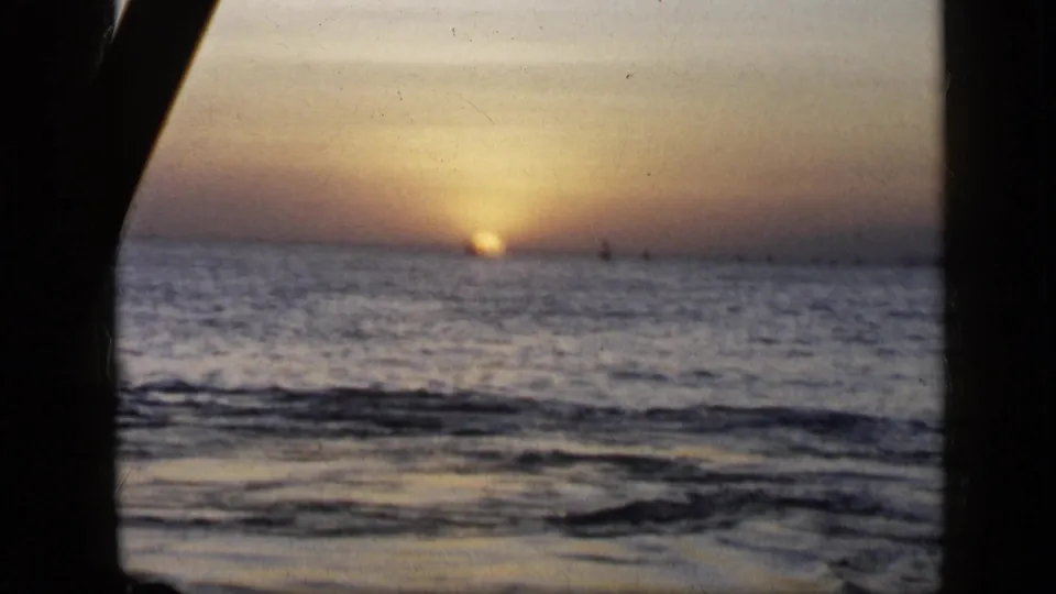 A second 1959 Venezuela home-movie view of the sun setting over rippled ocean water, with a dark frame edge at left.
