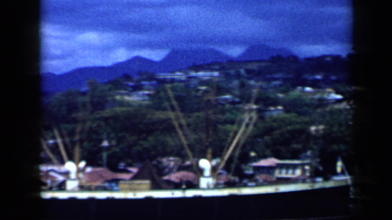 Venezuela coastal harbor view from the 1959 home movie, showing vessels near shore with hills and mountains in the distance.
