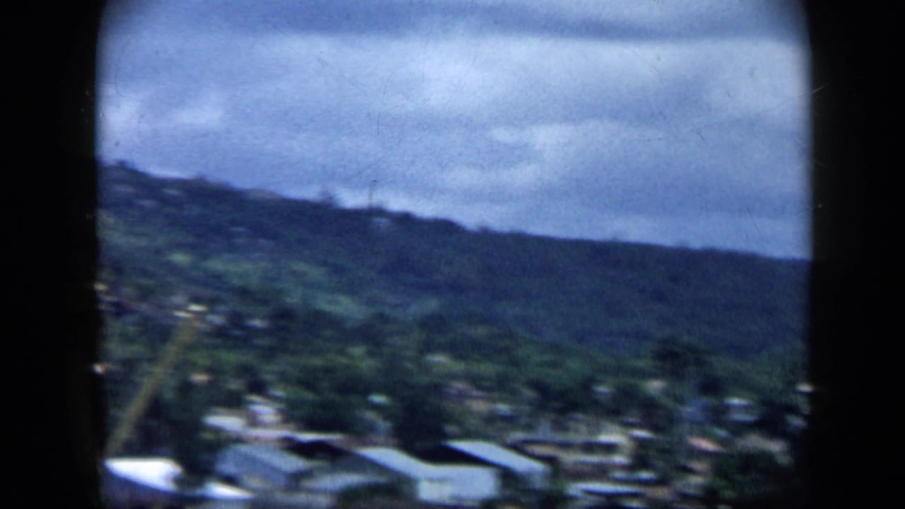 Soft 8mm view of green hills with scattered buildings under a cloudy sky.