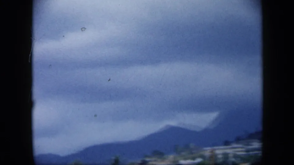 1959 Venezuela travel frame showing a dark mountain ridge, low clouds, and a small strip of buildings near the lower edge.