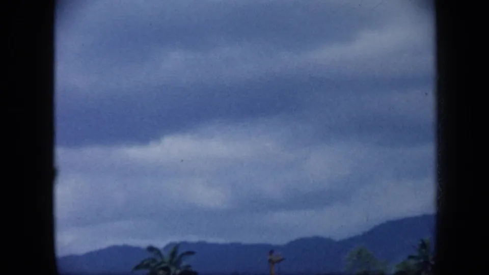 1959 Venezuela 8mm frame showing overcast mountains, a palm crown, and dark window-like borders around the view.