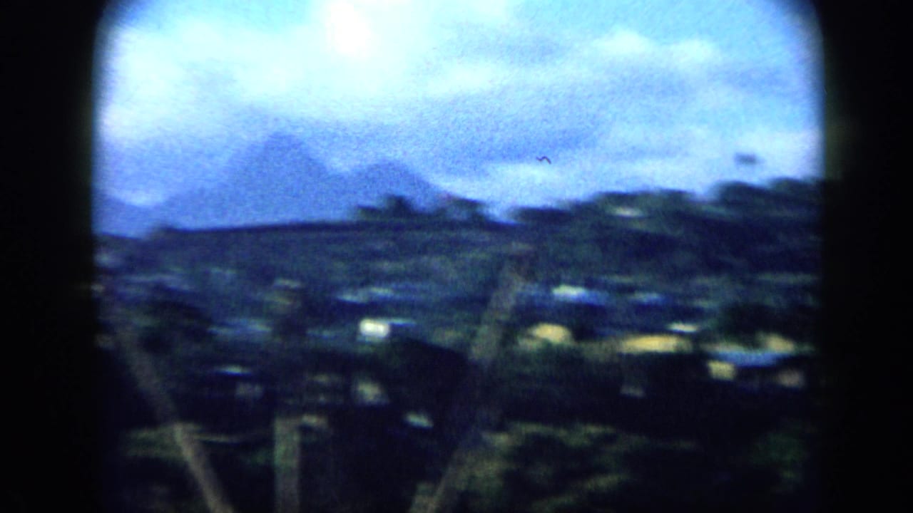 1959 Venezuela home-movie frame showing a blurred hillside landscape with scattered light structures and rounded 8mm frame edges.