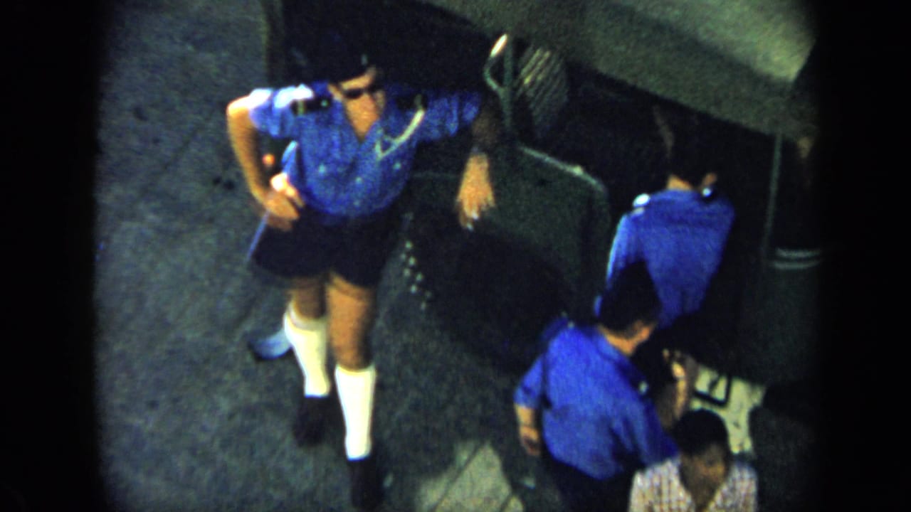 1959 Venezuela frame showing men in matching blue shirts and dark shorts on pavement, filmed from an elevated home-movie viewpoint.
