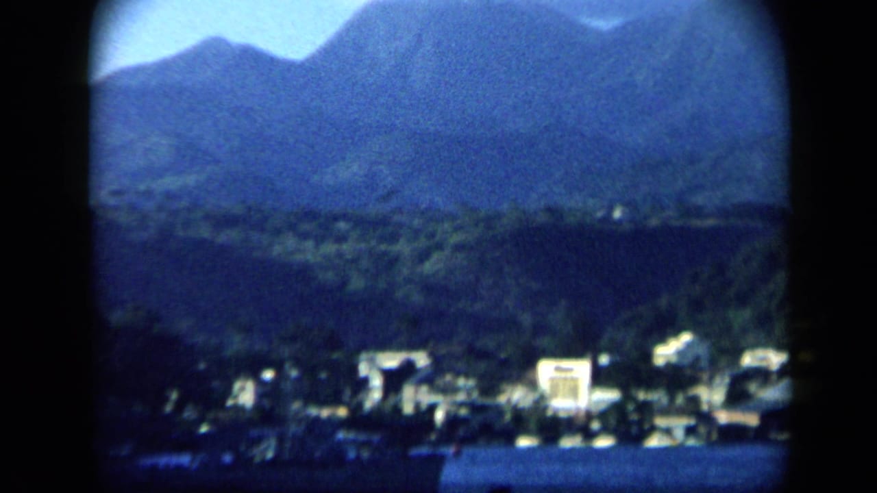 1959 Venezuela 8mm view of mountains, green hills, and distant town buildings across a harbor.