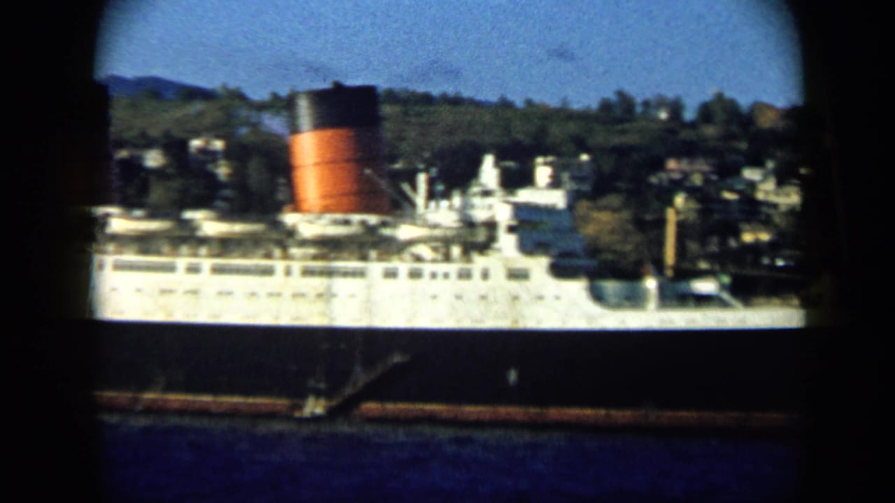 1959 Venezuela harbor shot showing a large white passenger ship with a red and black funnel before a hillside town.