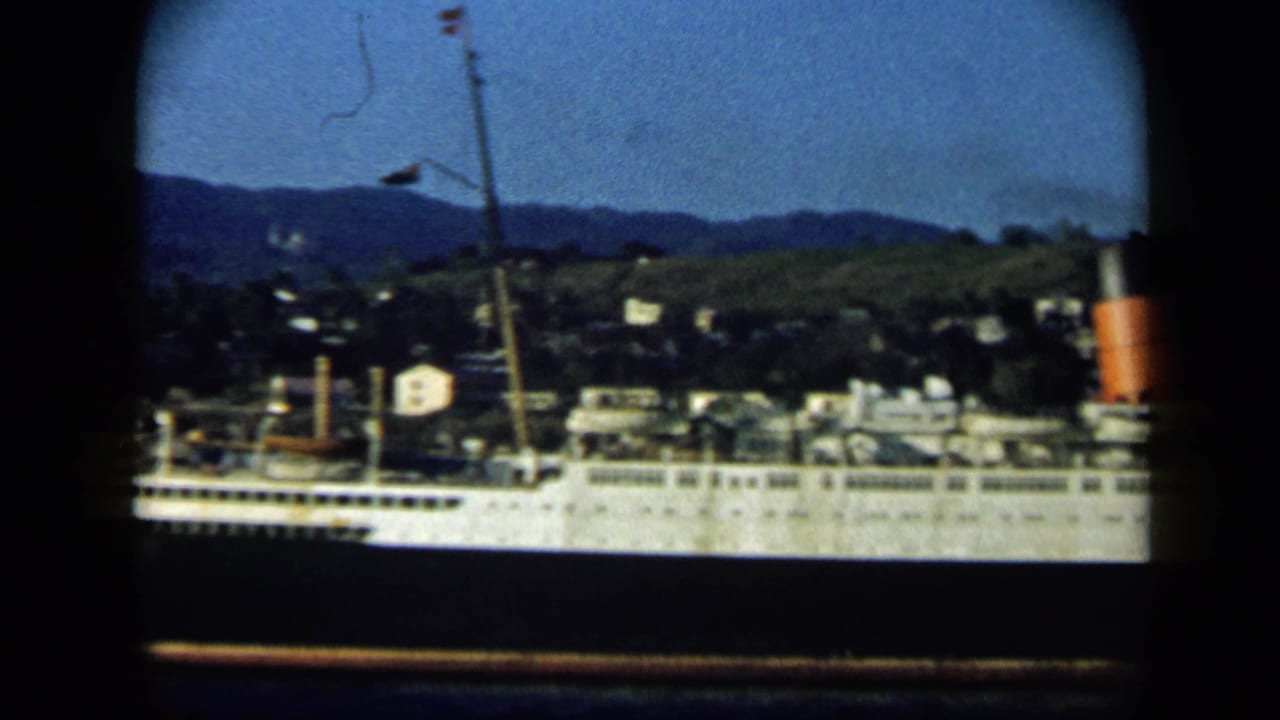 1959 Venezuela home-movie view of a passenger ship side, showing a mast, funnel, decks, and hillside townscape.