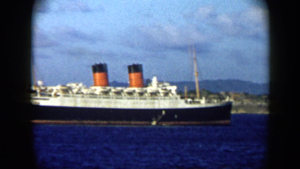 1959 Venezuela 8mm frame showing a large ocean liner passing across blue harbor water with low mountains in the background.