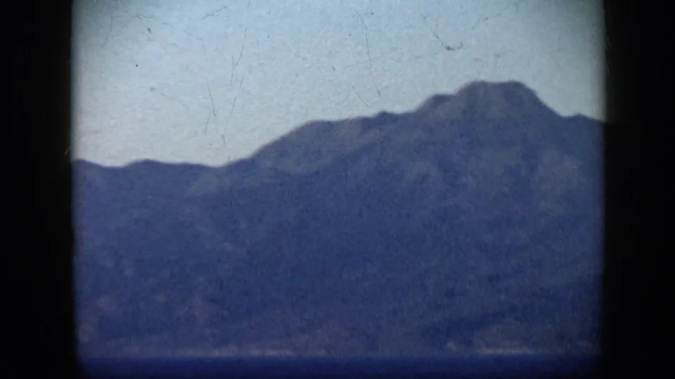 1959 Venezuela home-movie frame showing a hazy mountain profile across blue water, with the ship no longer visible.