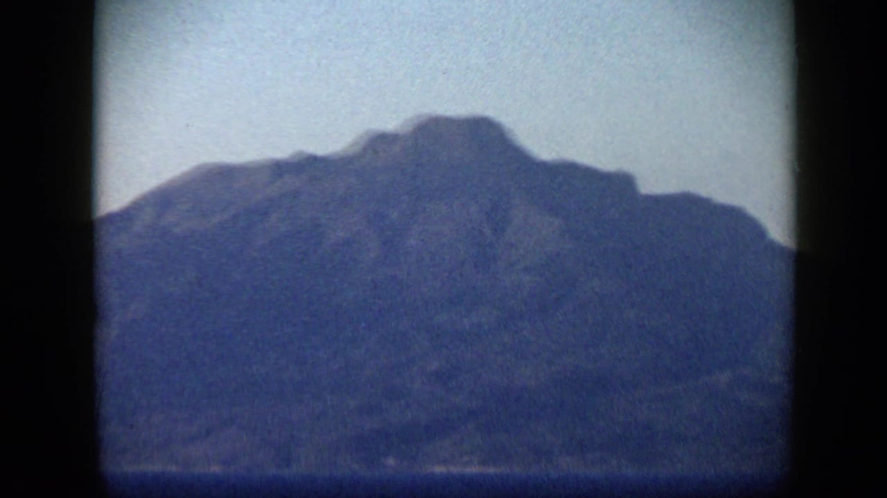 1959 Venezuela 8mm frame showing a dark mountain ridge across the horizon under a pale blue sky.
