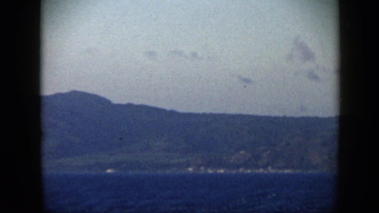 1959 Venezuela 8mm frame with low mountains, distant shoreline, dark water, and hazy sky.