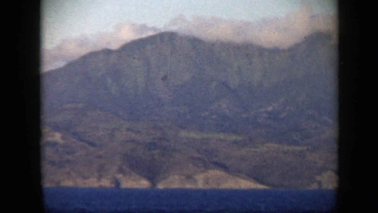 1959 Venezuela 8mm frame showing distant coastal mountains, pale clouds, and blue ocean seen through soft film grain.