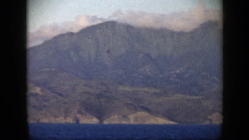 1959 Venezuela 8mm frame showing distant coastal mountains, pale clouds, and blue ocean seen through soft film grain.