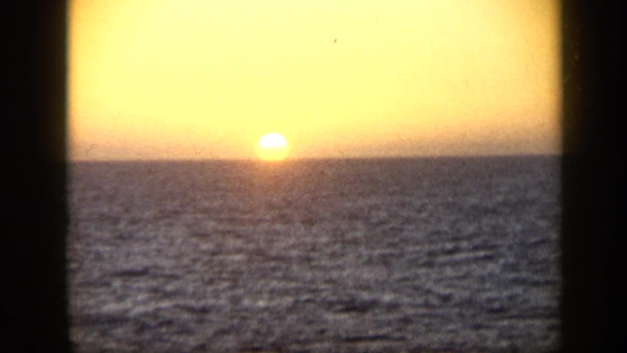 1959 Venezuela 8mm frame of the sun nearing the ocean horizon under a warm golden sky.