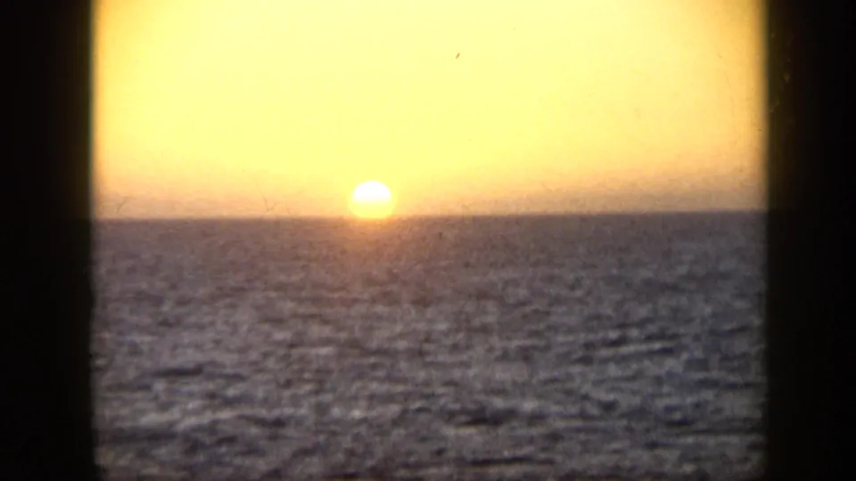 1959 Venezuela 8mm frame of the sun nearing the ocean horizon under a warm golden sky.