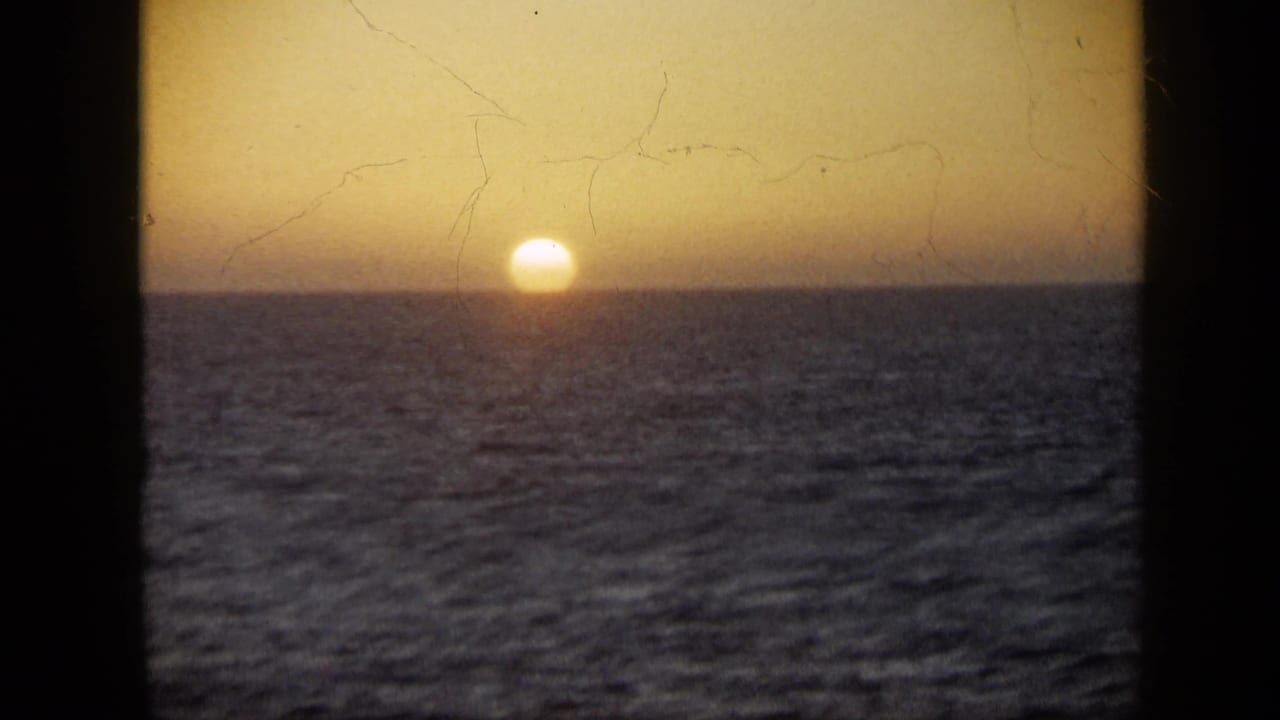 1959 Venezuela 8mm frame with the sun partly set at the sea horizon and scratches visible in the film surface.