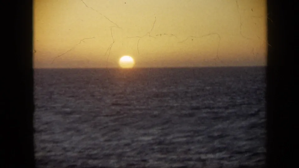 1959 Venezuela 8mm frame with the sun partly set at the sea horizon and scratches visible in the film surface.