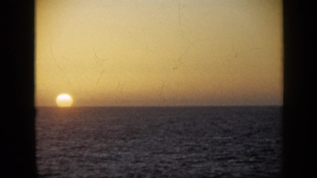 Golden sun near the ocean horizon beneath an amber sky, framed by dark 8mm film borders.