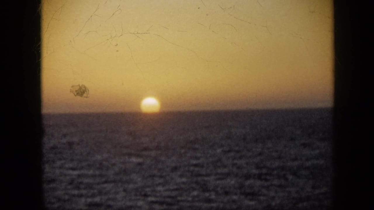 1959 Venezuela home-movie frame of a golden sun above the sea horizon, divided by dark 8mm frame borders.